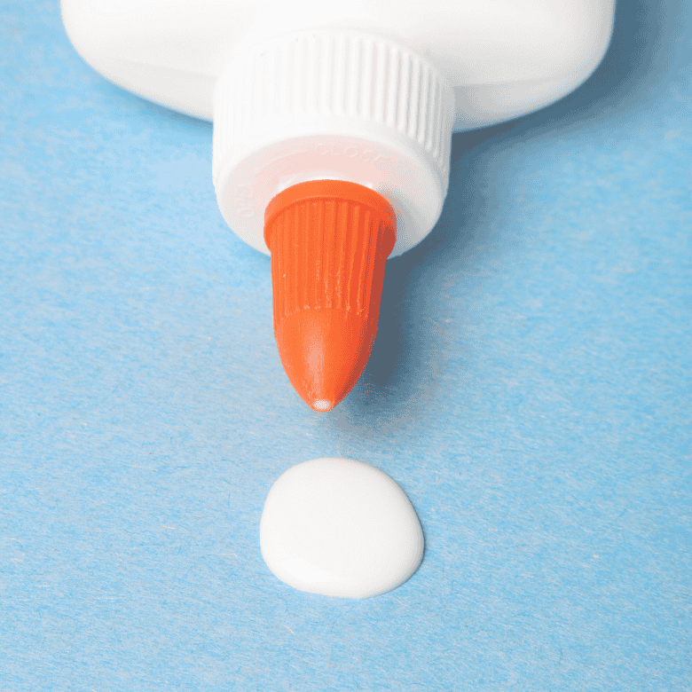 Weißer Schulkleber mit orangefarbener Spitze auf blauem Hintergrund.