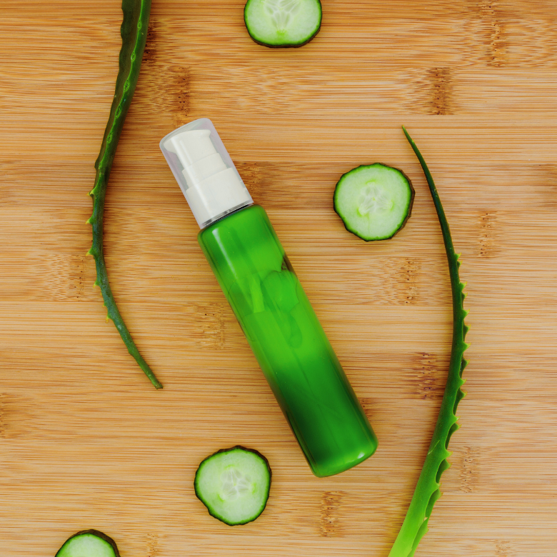 Green cosmetic bottle surrounded by cucumber slices and aloe vera leaves on a wooden background – natural skincare concept.
