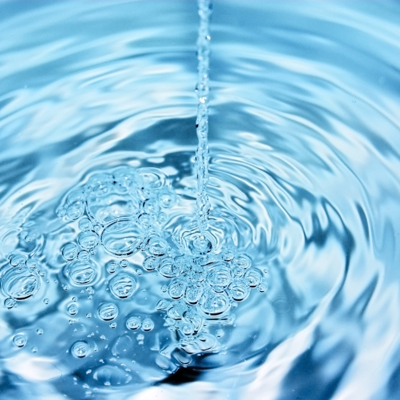 A stream of clean water falling into a blue surface, creating bubbles and ripples.