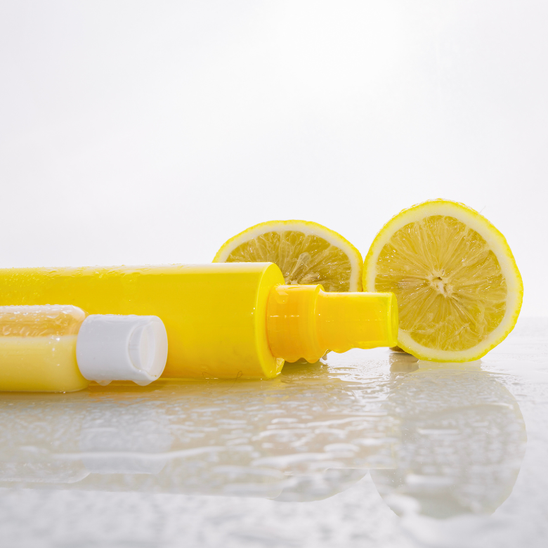 Yellow cosmetic bottles on a wet surface with lemon slices in the background – citrus-inspired skincare product.