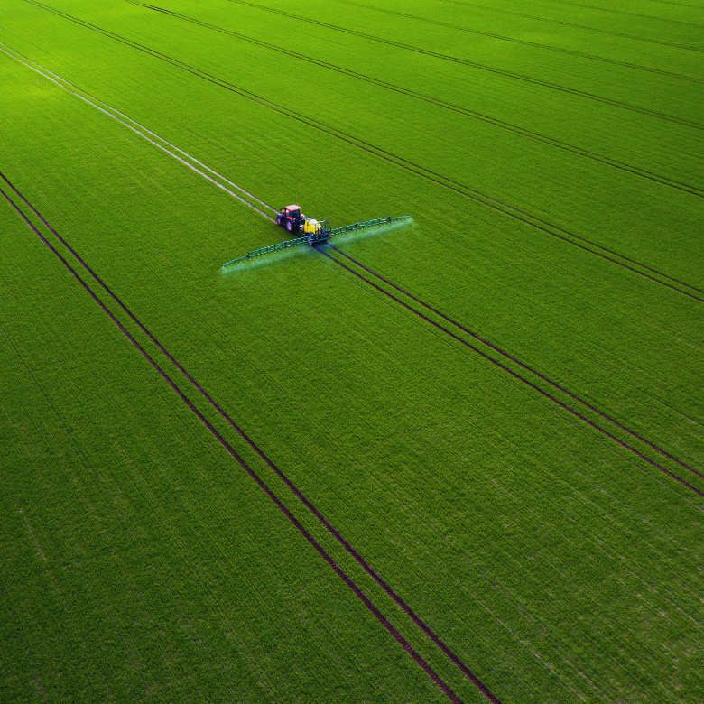 Agricultural machine spraying a large green crop field, aerial view.
