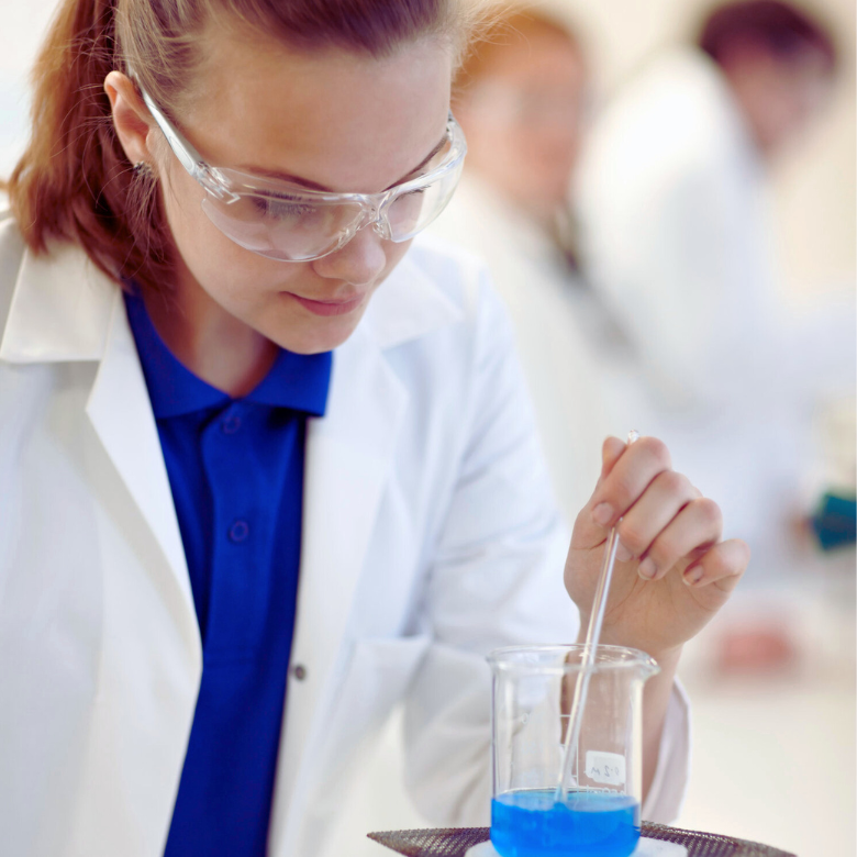 Kobieta w okularach ochronnych miesza niebieską ciecz w zlewce podczas pracy w laboratorium.