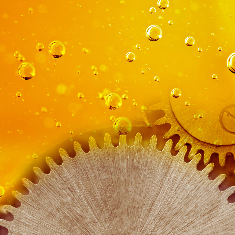 Close-up of metal gears immersed in golden oil with visible air bubbles.
