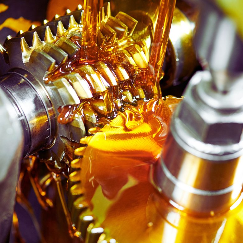 Close-up of metal gears being lubricated with golden oil flowing over the mechanism’s components.